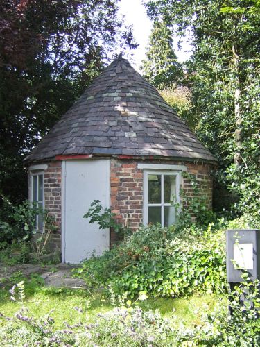 A circular brick-built structure with a conical slate roof surrounded by greenery..