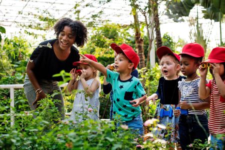 A teacher and schoolchildren explore plants in a large greenhouse.