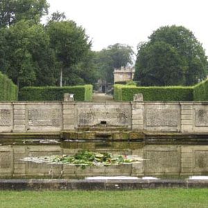 A water feature in front of a stone wall in a designed garden.