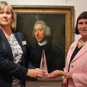 Two women stand in front of a portrait of Lancelot 'Capability' Brown.