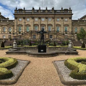 The facade of a grand stately home with geometric formal gardens in the foreground.