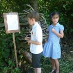Schoolchildren read an information sign on a wooden post.