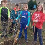 Children stand by an apple tree they have just planted.